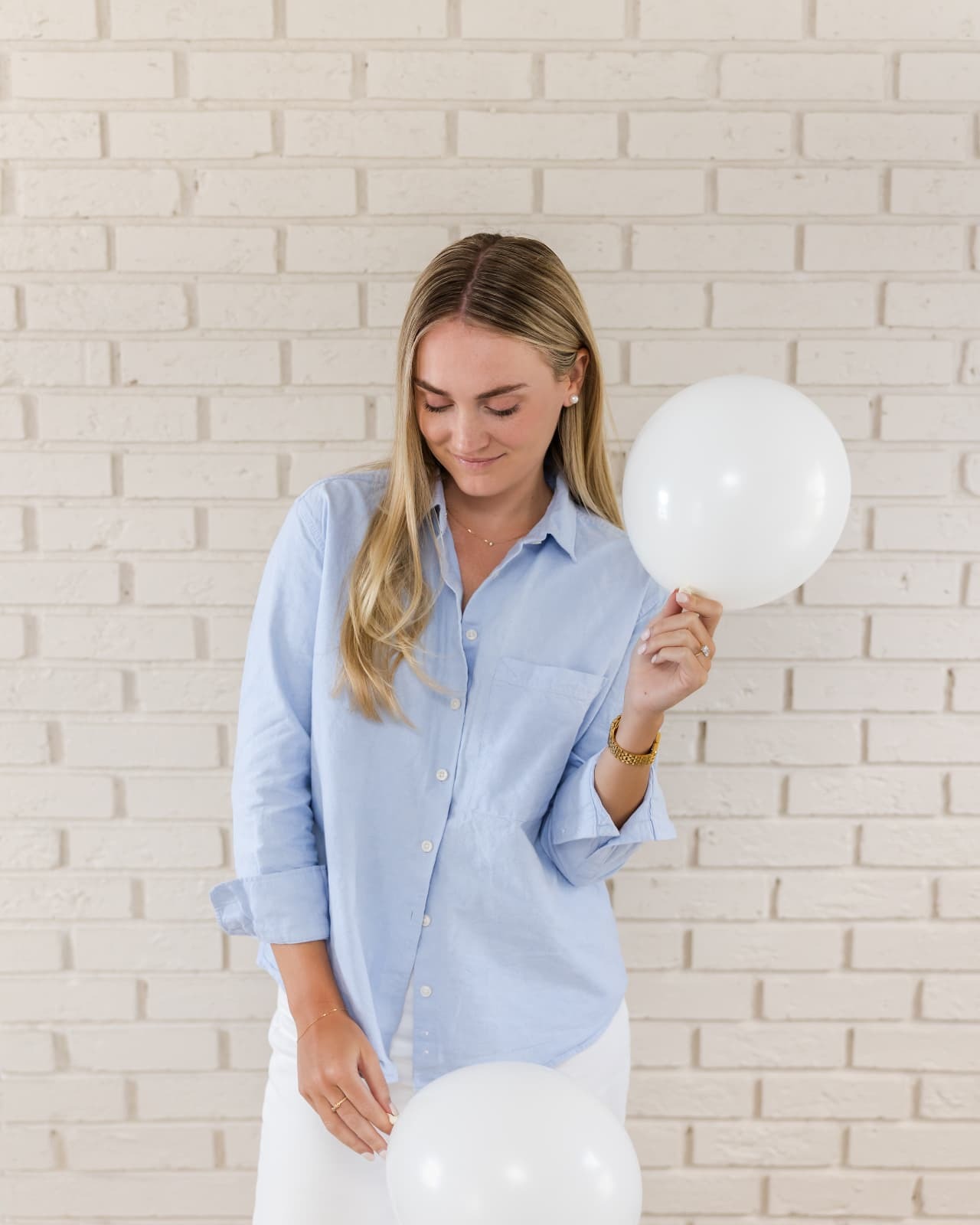 Lily holding white balloons against a painted brick wall